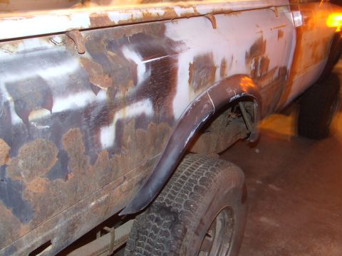1990 Ford Bronco - The side of a heavily rusted vehicle shows primer spots and a damaged fender flare.