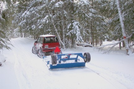 1987 Suzuki Samurai - A red 1987 Suzuki Samurai equipped with snow tracks navigates a snow-covered path while towing a blue implement.