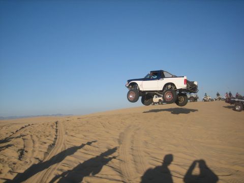 1995 Ford Bronco - This modified 1995 Ford Bronco is airborne over a sand dune, with other off-road vehicles visible.
