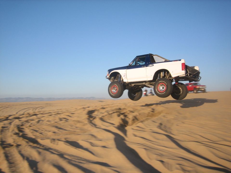 lifted pickup truck mid-air over sand dunes, another car in background