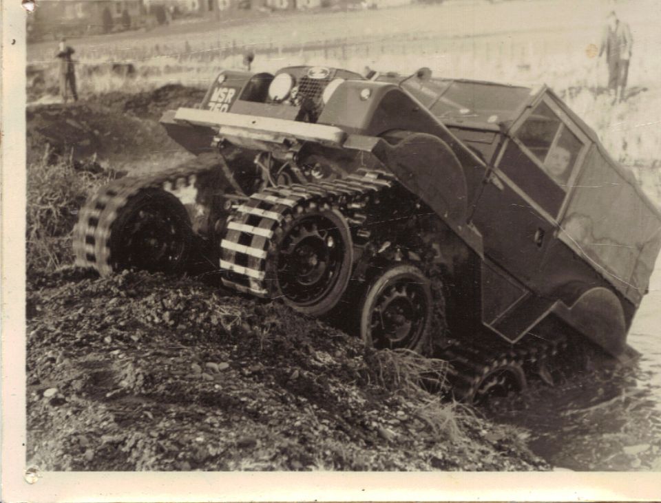 Vintage tracked vehicle on muddy terrain with visible bogie wheels and driver in cab