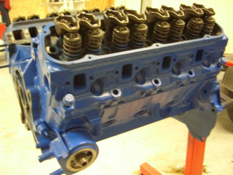 1996 Ford Bronco - A freshly painted blue V8 engine block is displayed on a stand, ready for assembly.