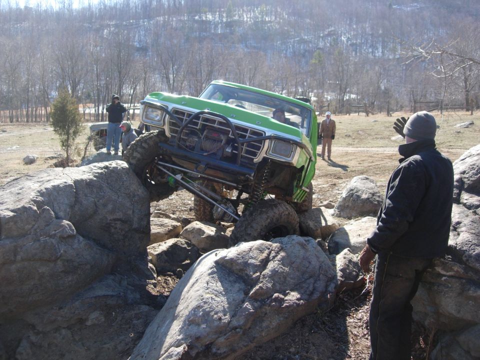 Green and white Ford Bronco with winch bumper climbing boulders as a spotter watches