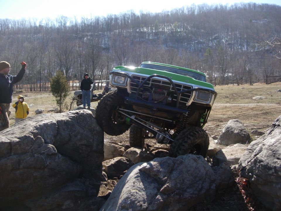 Green and white 1970s Ford 4x4 with winch bumper crawling a rock ledge, front wheel flexed