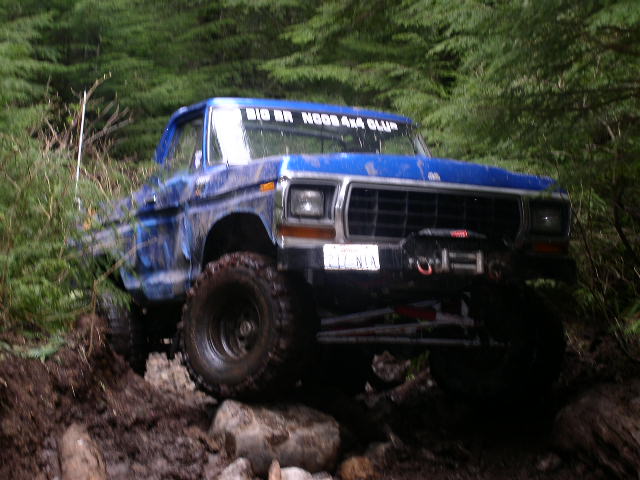 Blue 1979 Ford Bronco with large tires on a muddy, rocky trail