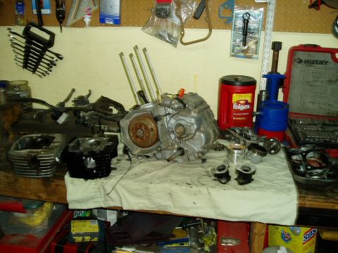 2000 Ford E350 - Disassembled motorcycle engine components laid out on a workbench, alongside tools and a Folgers coffee can.