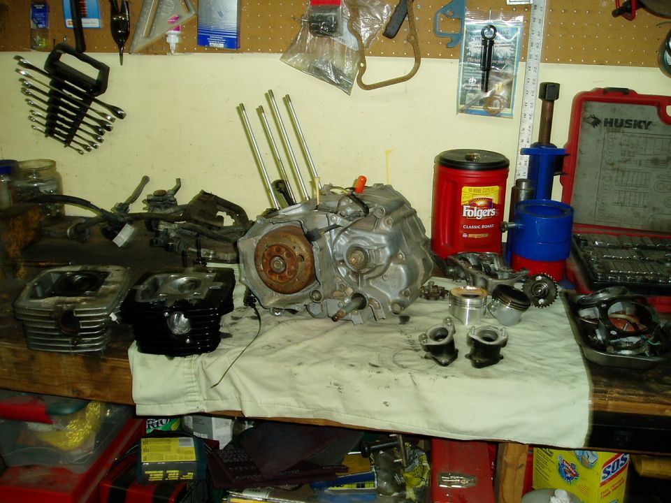 Motorcycle engine disassembled on a workbench with tools and coffee can