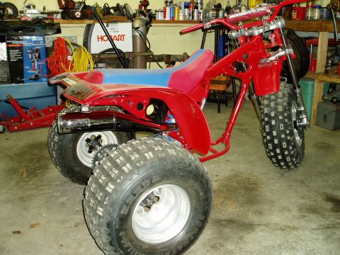 2000 Ford E350 - A red three-wheeled ATV is parked in a garage, showing its frame, seat, and large tires.