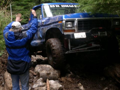1979 Ford Bronco - Blue 1979 Ford Bronco navigating a rocky, muddy trail with a person assisting.