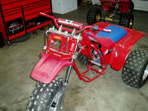 2000 Ford E350 - A red Honda three-wheeler with a blue seat and Moose Racing handlebars is parked in a garage next to another ATV.