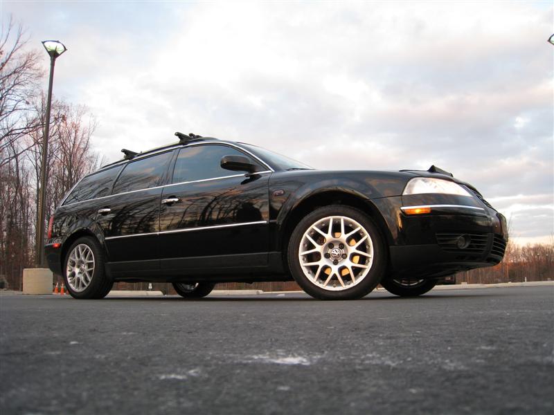 Low-angle front three-quarter of a black VW Passat wagon with mesh alloys and roof rack in a parking lot