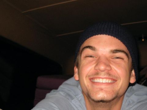 1989 Ford Bronco - A man with a beard and a beanie smiles broadly inside a dimly lit space.