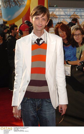 1989 Ford Bronco - A man in a white blazer and a colorful striped sweater stands on a red carpet event.