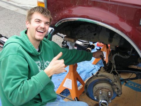 1989 Ford Bronco - A man smiles while working on the suspension of a red vehicle, which is supported by jack stands.
