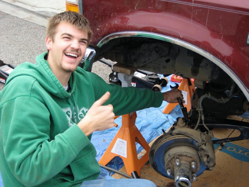 Man working on red vehicle's front suspension, giving thumbs up