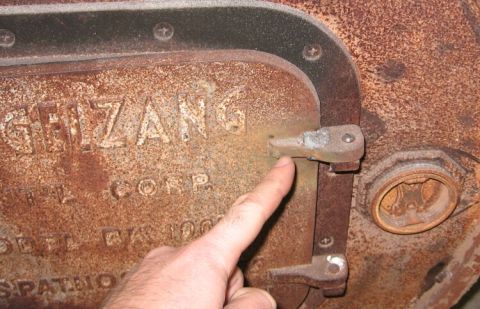 1986 Ford Ranger - A finger points to a latch on a heavily rusted metal plate with embossed text, possibly from an old machine.