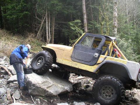 1979 Ford Bronco - Off-road Jeep Wrangler tackling a challenging rocky trail with a person observing.