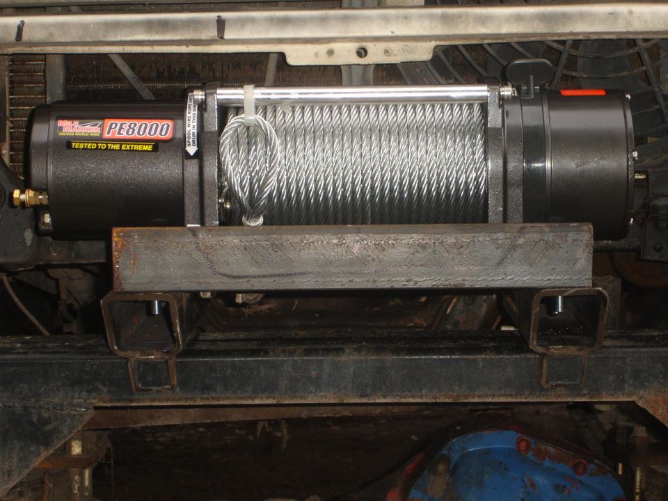 Winch with PE8000 label mounted on metal brackets attached to vehicle frame