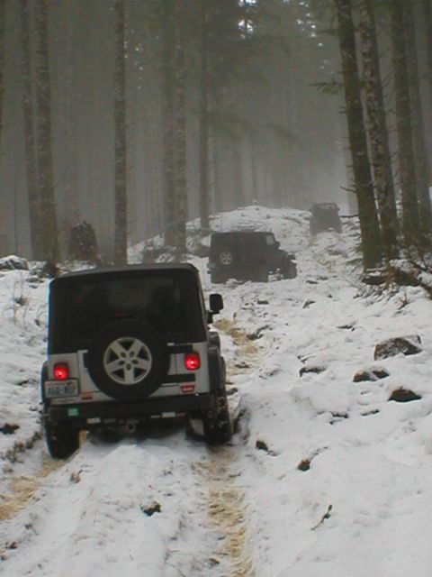 2005 Jeep Wrangler - Two Jeep Wranglers navigate a snowy path through a forest, suggesting off-road adventure in winter conditions.