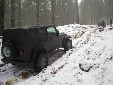 2005 Jeep Wrangler - A Jeep Wrangler navigates a snowy trail through a forest, with two people visible in the distance.
