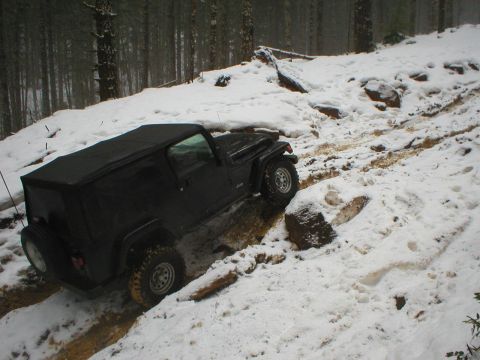 2005 Jeep Wrangler - A black Jeep Wrangler navigates a muddy and snowy trail through a forest.
