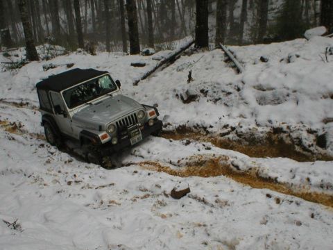 2005 Jeep Wrangler - Jeep Wrangler navigating a challenging snowy and muddy path through a wooded area.