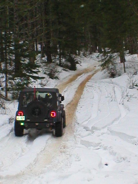 2005 Jeep Wrangler - A black Jeep Wrangler navigates a snow-covered path through a forest.