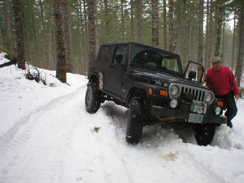 2005 Jeep Wrangler - A black 2005 Jeep Wrangler navigates a snowy forest road with a person standing by the open driver's door.