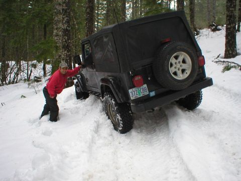 2005 Jeep Wrangler - Person poses with a black Jeep Wrangler as it drives through deep snow in a forest.