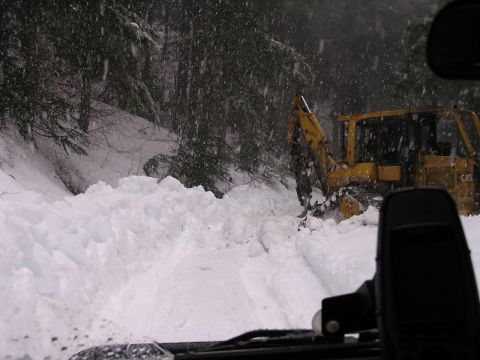2005 Jeep Wrangler - Shot through a windshield in falling snow, a yellow Caterpillar tracked excavator clears a deep snowbank blocking a forest road. The vehicl…