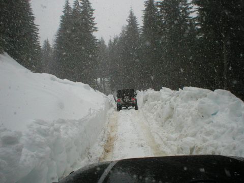 2005 Jeep Wrangler - A black Jeep Wrangler navigates a narrow path through deep snowdrifts on a wooded road during a snowstorm.