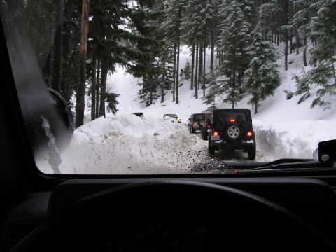 2005 Jeep Wrangler - Multiple Jeep Wranglers navigate a snow-covered mountain road, viewed from the driver's perspective.