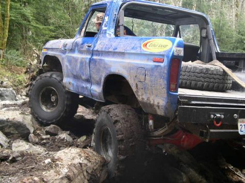 1979 Ford Bronco - A blue off-road truck is shown traversing a challenging rocky path.