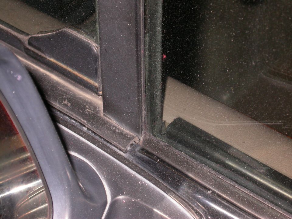 Close-up of a vehicle's door frame and window seal, showing rubber trim and metal components