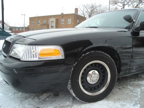 2000 Ford Crown Victoria - The front fender and headlight assembly of a black sedan are visible in this close-up shot.