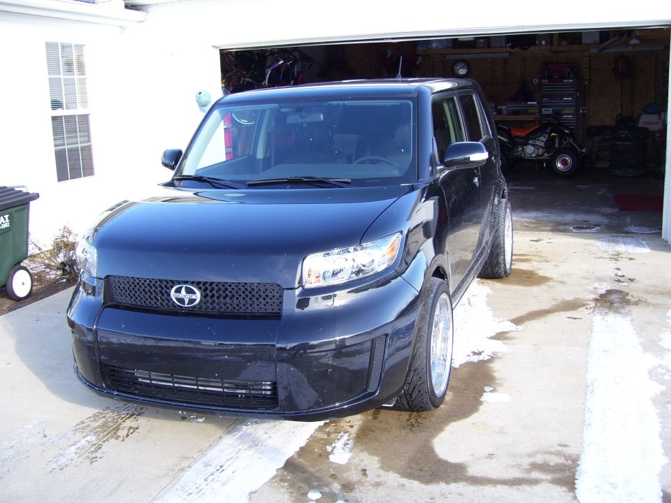 Black Scion xB front three-quarter view in a driveway near an open garage