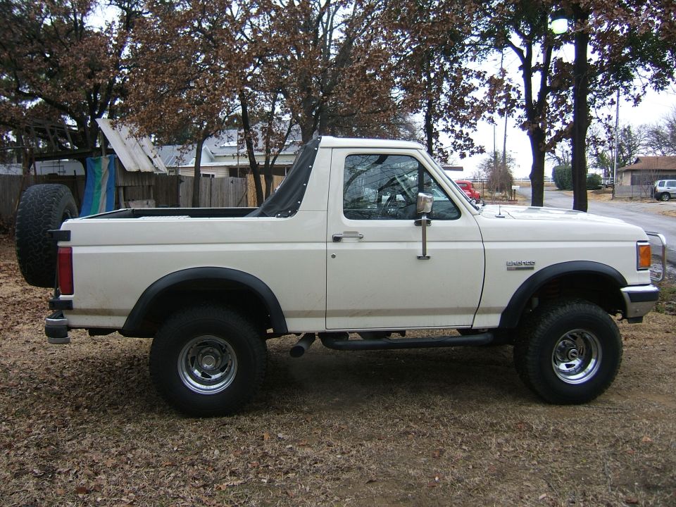 White Ford Bronco with top removed, side view, roll bar, chrome wheels and side steps