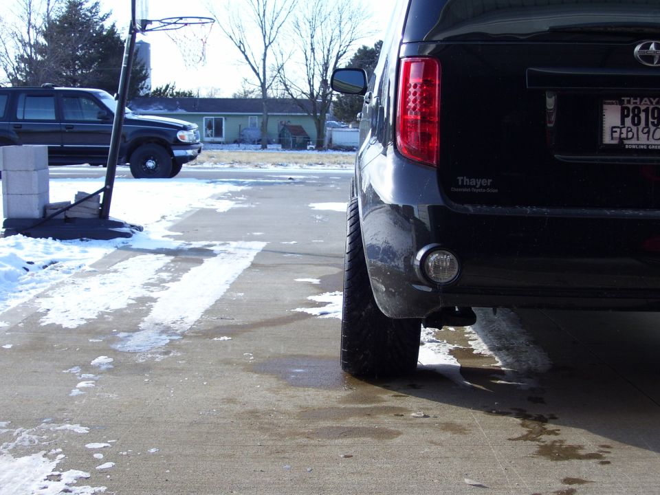 Rear driver side of black Scion xB on snowy driveway with dealer badge and plate.