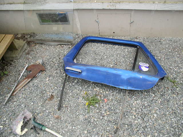 Blue Ford Bronco door propped on gravel mid-modification with tools nearby