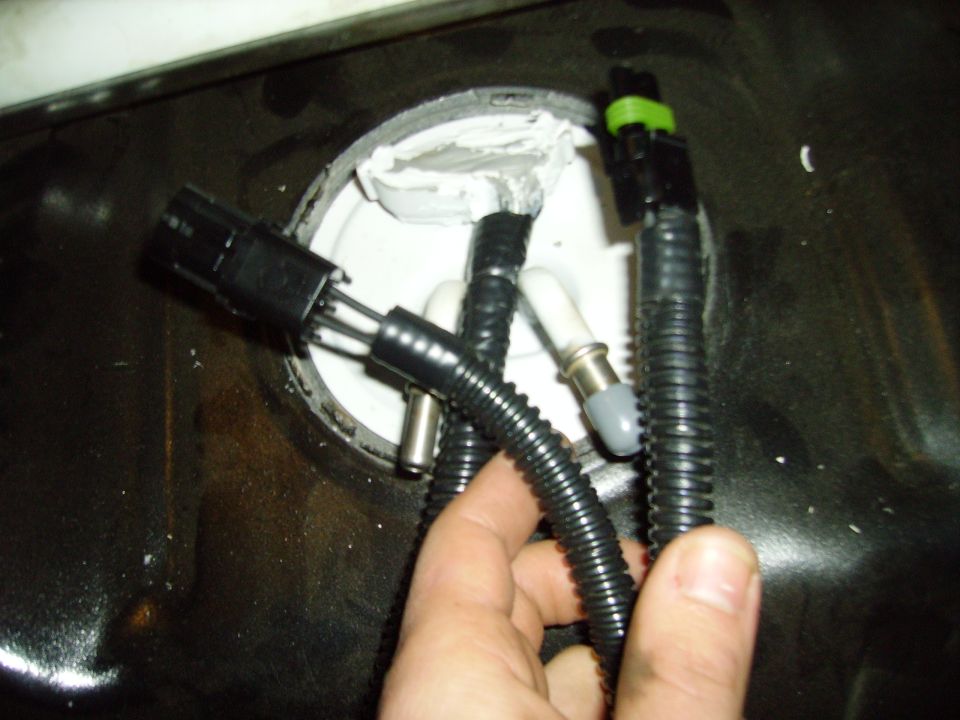 Hand holding fuel pump electrical connector and hoses near fuel tank opening