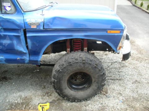 1979 Ford Bronco - Close-up of a blue 1979 Ford Bronco's side, showing a damaged fender and a large tire.