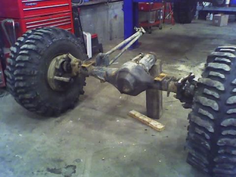 1992 Ford Bronco - The rear axle and massive tires of a vehicle are shown in a workshop setting, possibly undergoing maintenance.