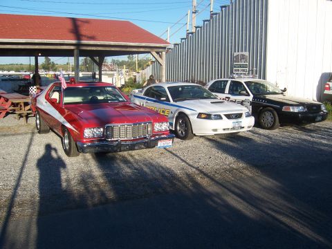 1975 Ford Torino - A red and white 1976 Ford Gran Torino is parked next to a white police car and a black police car.