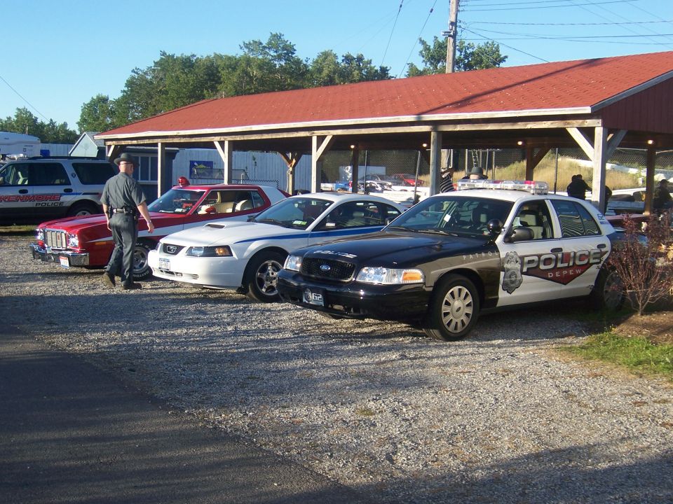 Police car with "POLICE DEPEW" text, parked next to a white Ford Mustang and a red coupe