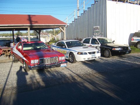 1975 Ford Torino - A 1975 Ford Torino is parked alongside two police vehicles under a covered area.