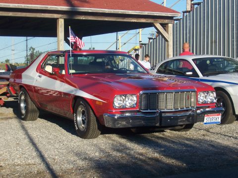 1975 Ford Torino - A red and white Ford Gran Torino is parked outdoors, with an American flag on its antenna.