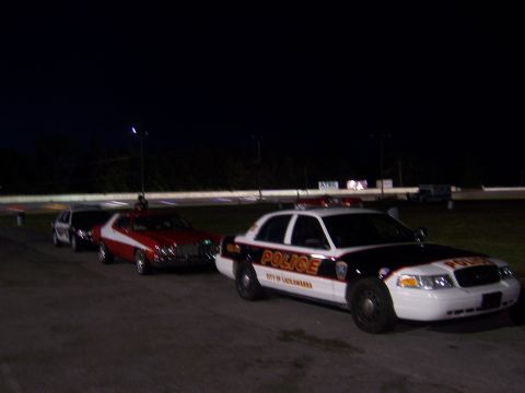 1975 Ford Torino - A red and white 1975 Ford Torino is parked behind a police car at night.