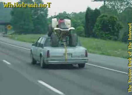 1989 Ford Bronco - An ATV is precariously strapped to the roof of a sedan on the highway.