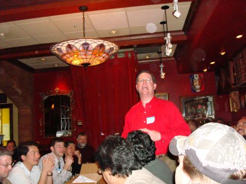 1990 Ford Bronco - A group of people are gathered in a room, with one man in a red shirt addressing them.