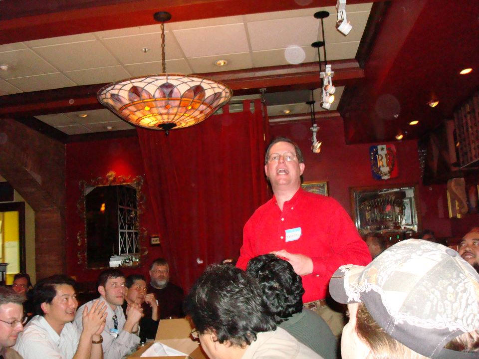 People gathered in a room with a man in a red shirt speaking